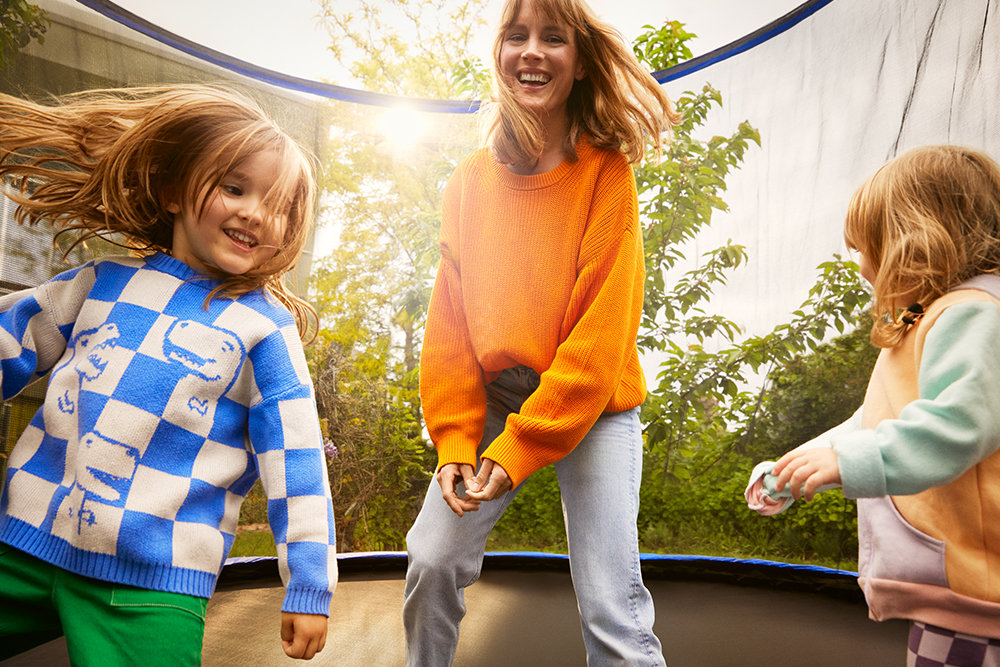 Mutter hüpft mit ihren zwei Töchtern auf einem Trampolin im Garten ihres neuen Zuhauses.