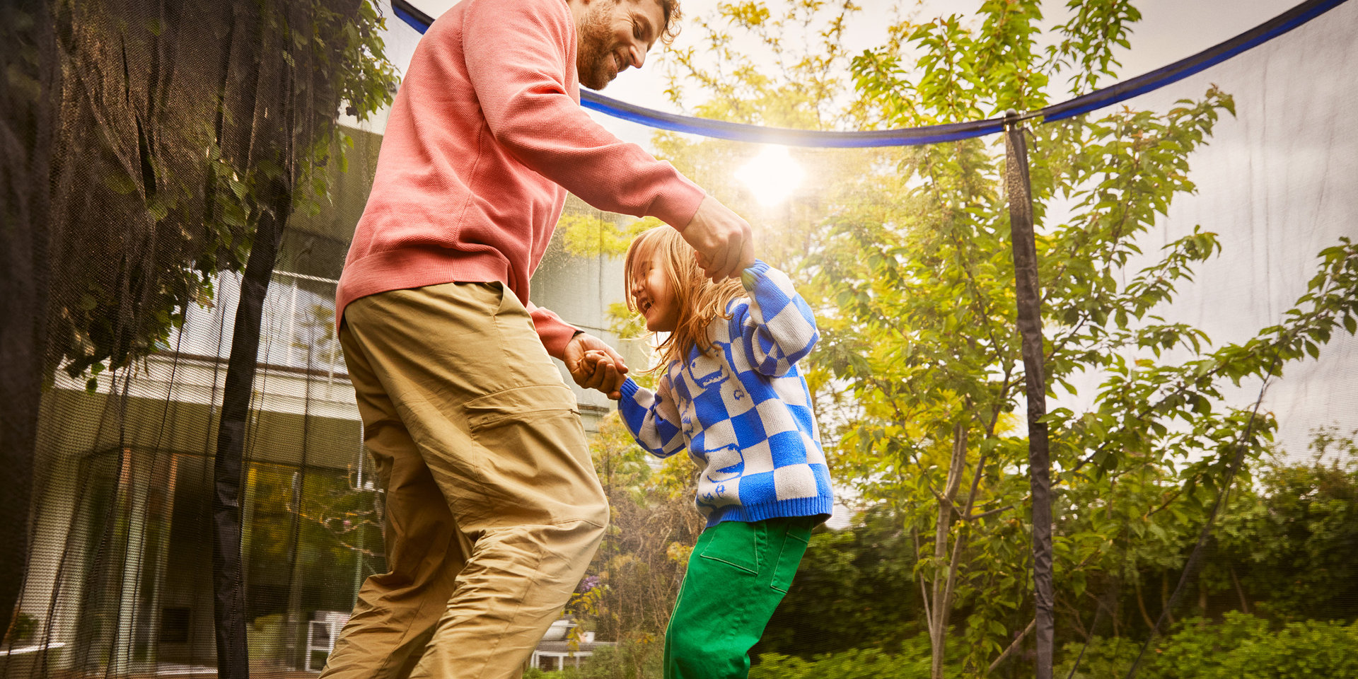 Vater und Tochter halten sich an den Händen und springen auf einem Trampolin im Garten ihres neuen Zuhauses. 