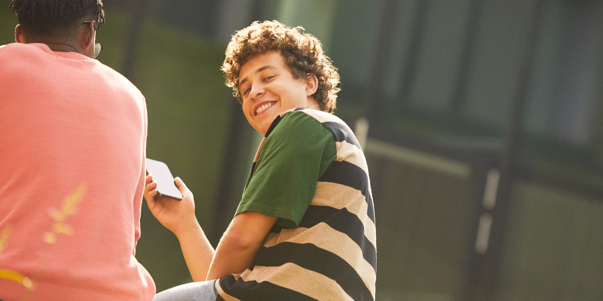 Wüstenrot Lehrling hält lächelnd sein Smartphone in der Hand und blickt über seine Schulter zurück