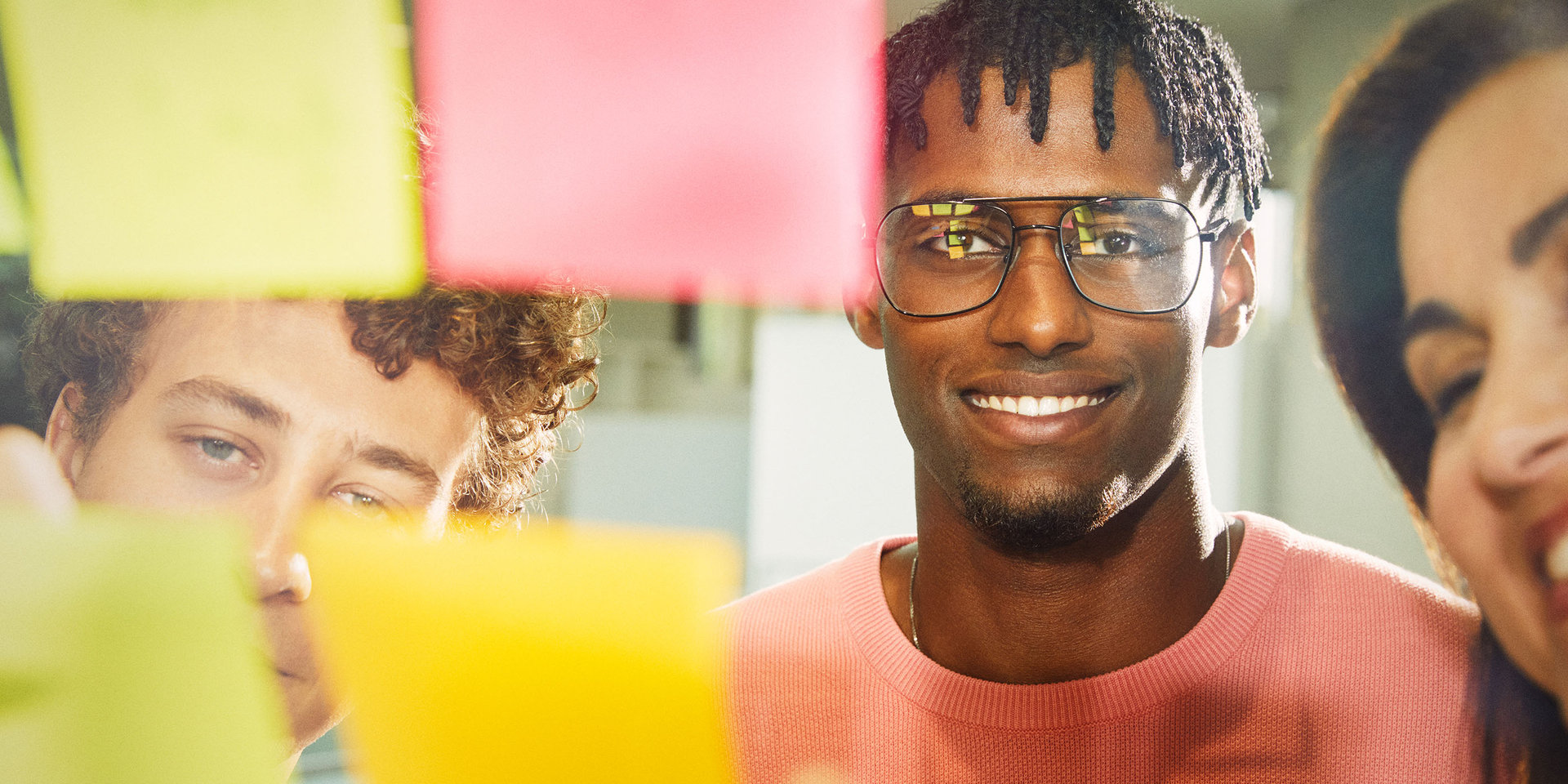 Zwei Mitarbeiter und eine Mitarbeiterin bei Wüstenrot vor einer Postit-Wand beim Brainstorming