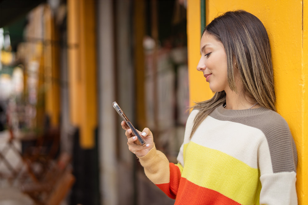 Eine Frau lehnt entspannt an der Wand und blickt auf ihr Handy.