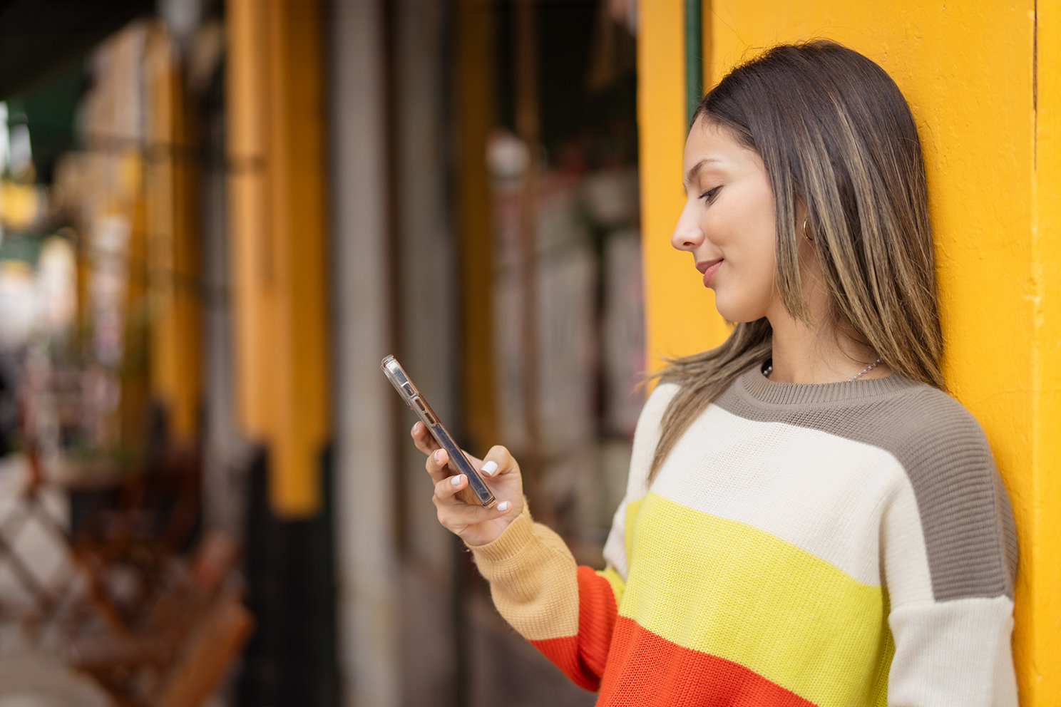 Eine Frau lehnt entspannt an der Wand und blickt auf ihr Handy.