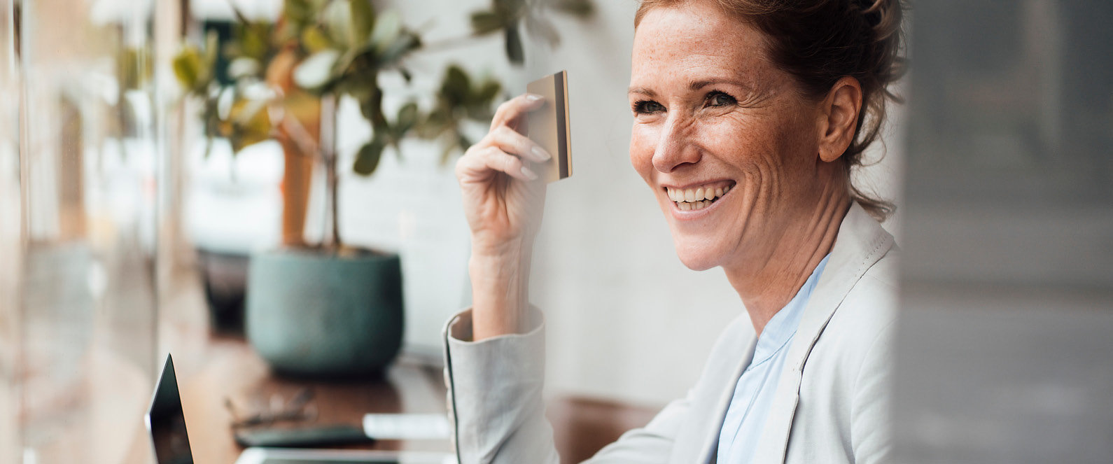 Frau hält lächelnd eine Bankomatkarte in der Hand.