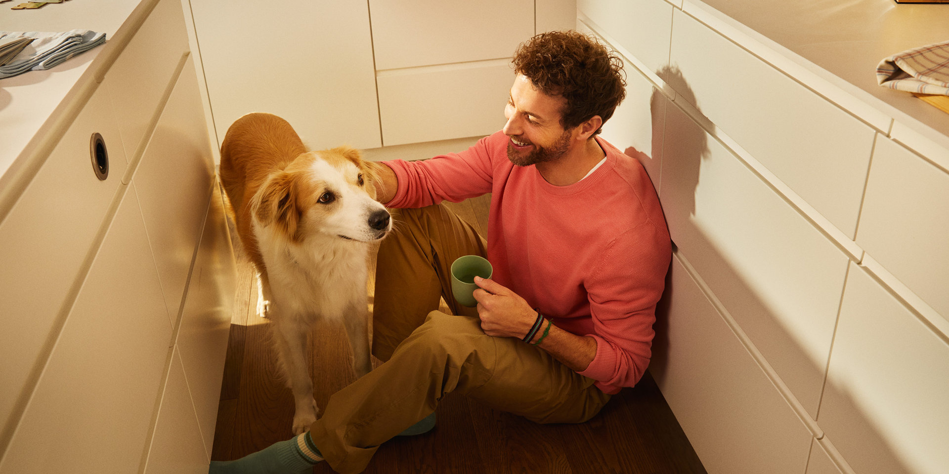 Mann sitzt mit Hund am Boden in der Küche Mann sitzt mit Hund am Boden in der Küche