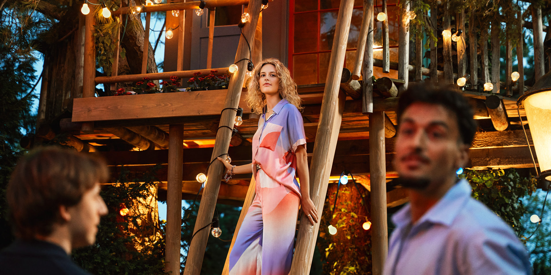 Eine blonde Frau steht bei einer Party auf der Treppe eines Baumhauses.