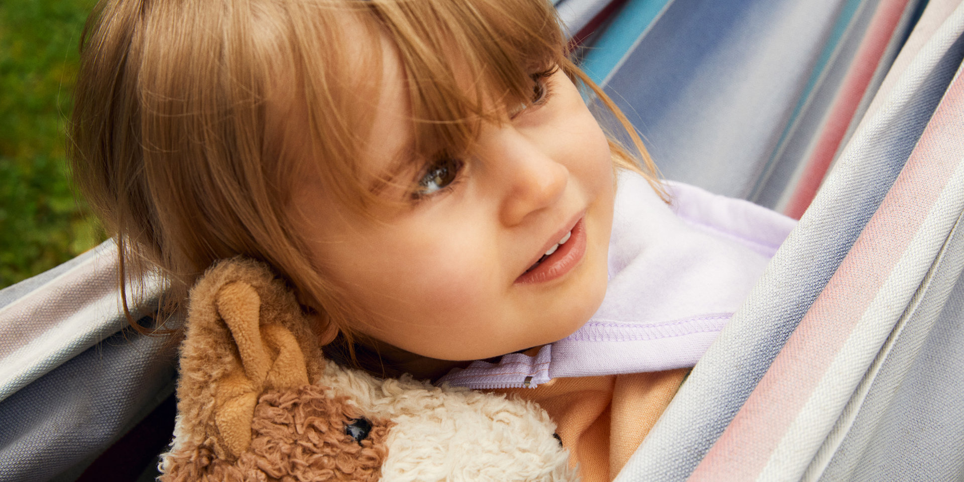 Ein kleines Mädchen sitzt mit ihrem Kuscheltier in der Hängematte.