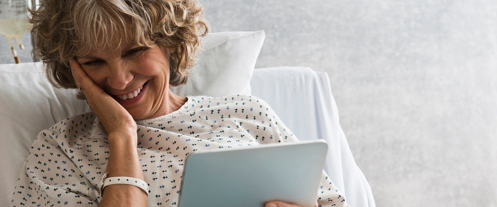 Ältere Frau liegt im Krankenhausbett und freut sich, durch ihre Gesundheitsvorsorge von Wüstenrot gut abgesichert zu sein.