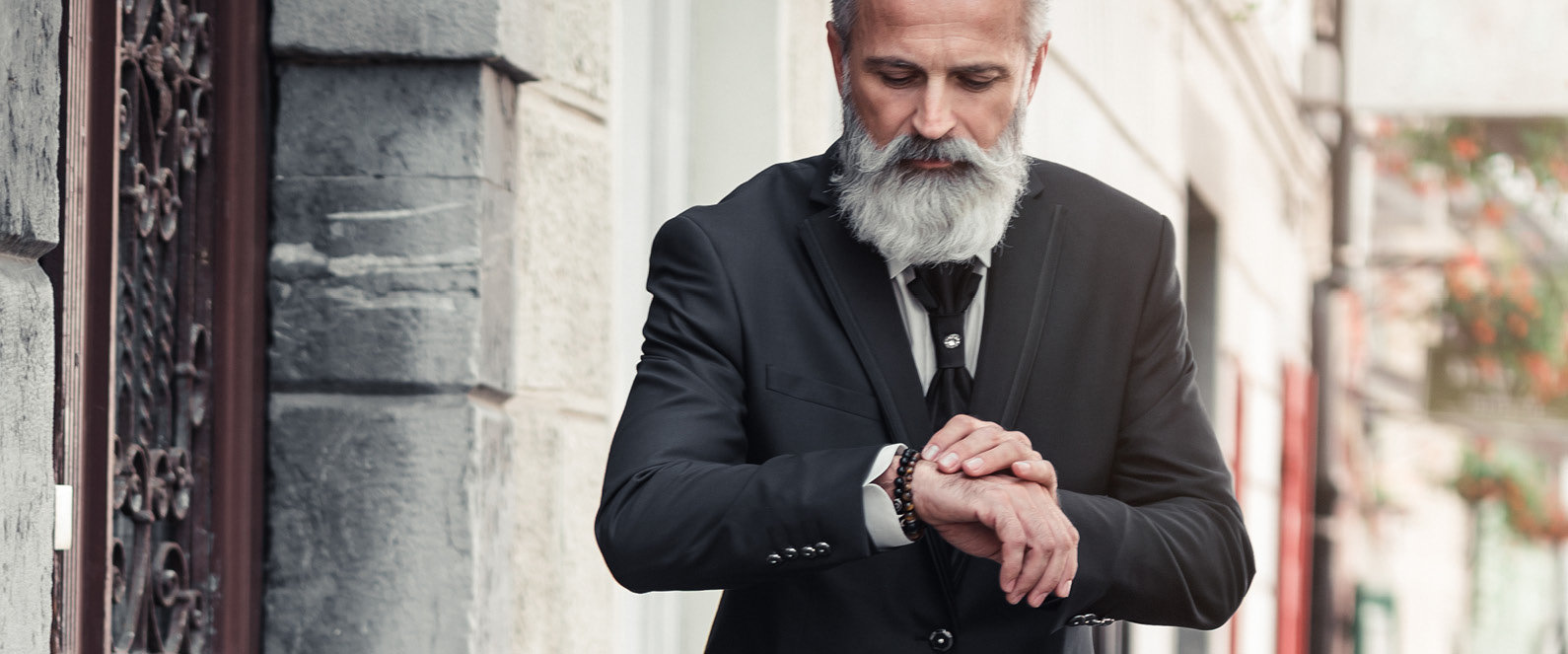 Ein älterer Mann mit weißem Bart blickt auf seine Uhr.