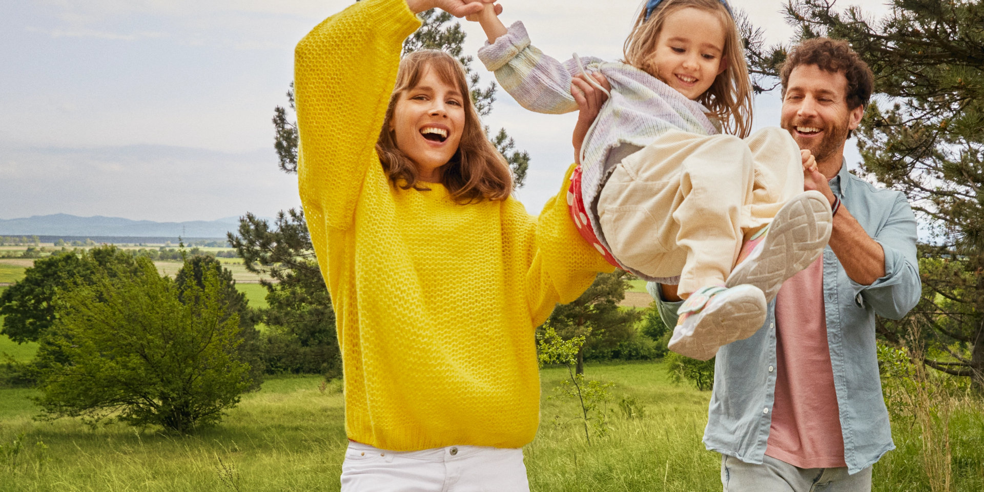 Eine Frau und ein Mann spielen sorgenfrei mit ihrem Kind in der Natur. 