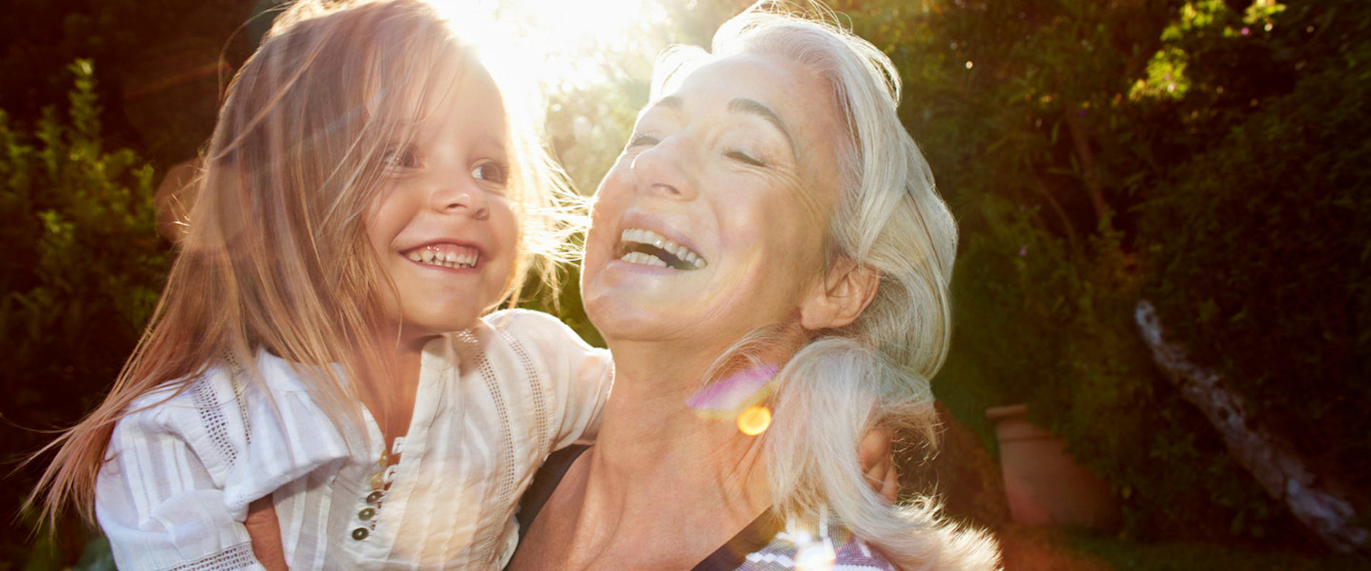 Eine ältere Frau hält lachend ihr Enkelkind auf dem Arm und freut sich, dass sie für ihre Pension finanziell vorgesorgt hat.