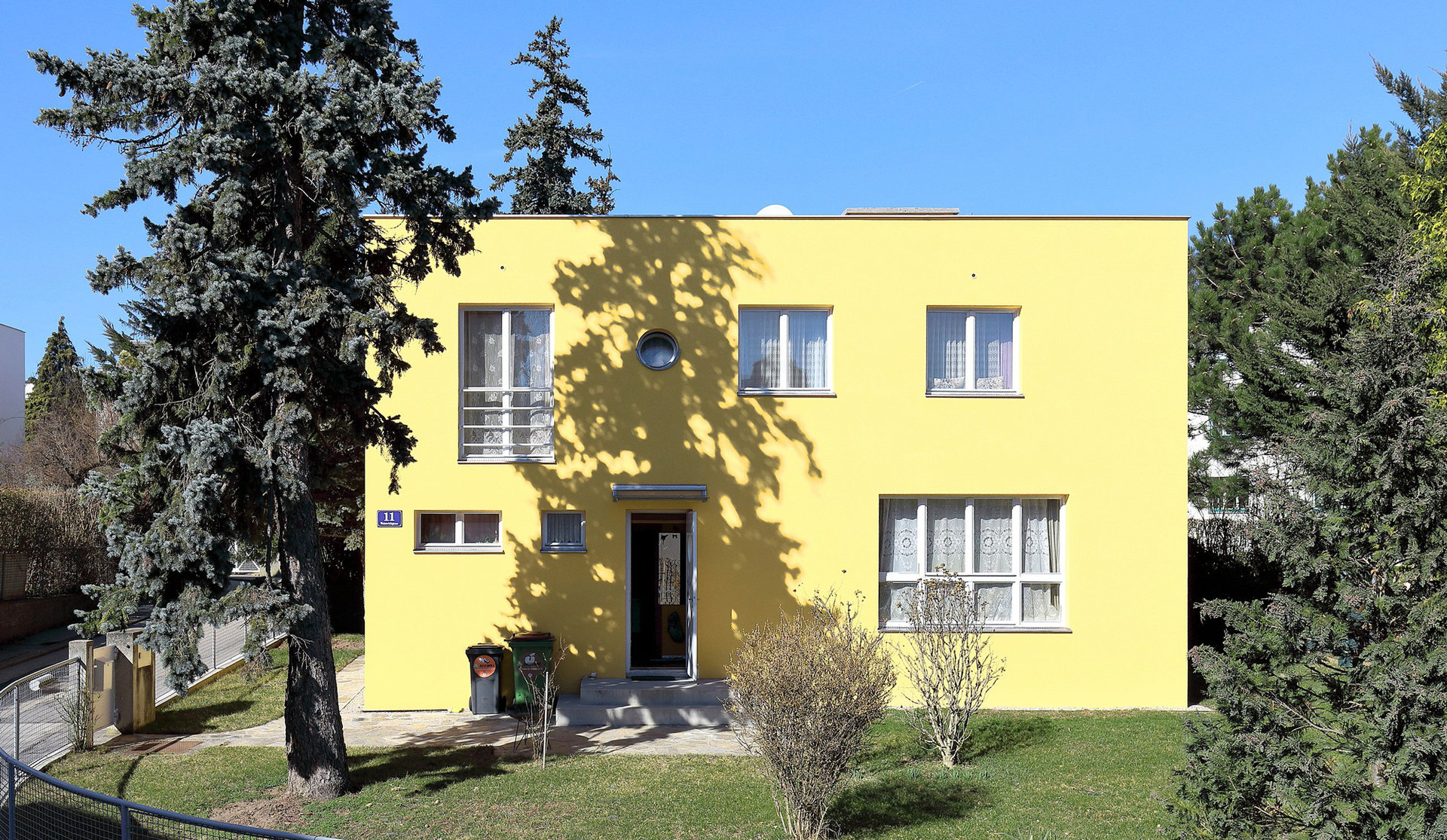 Gelbes Wohnhaus in der Sonne, davor ein Baum der einen Schatten auf das Haus wirft
