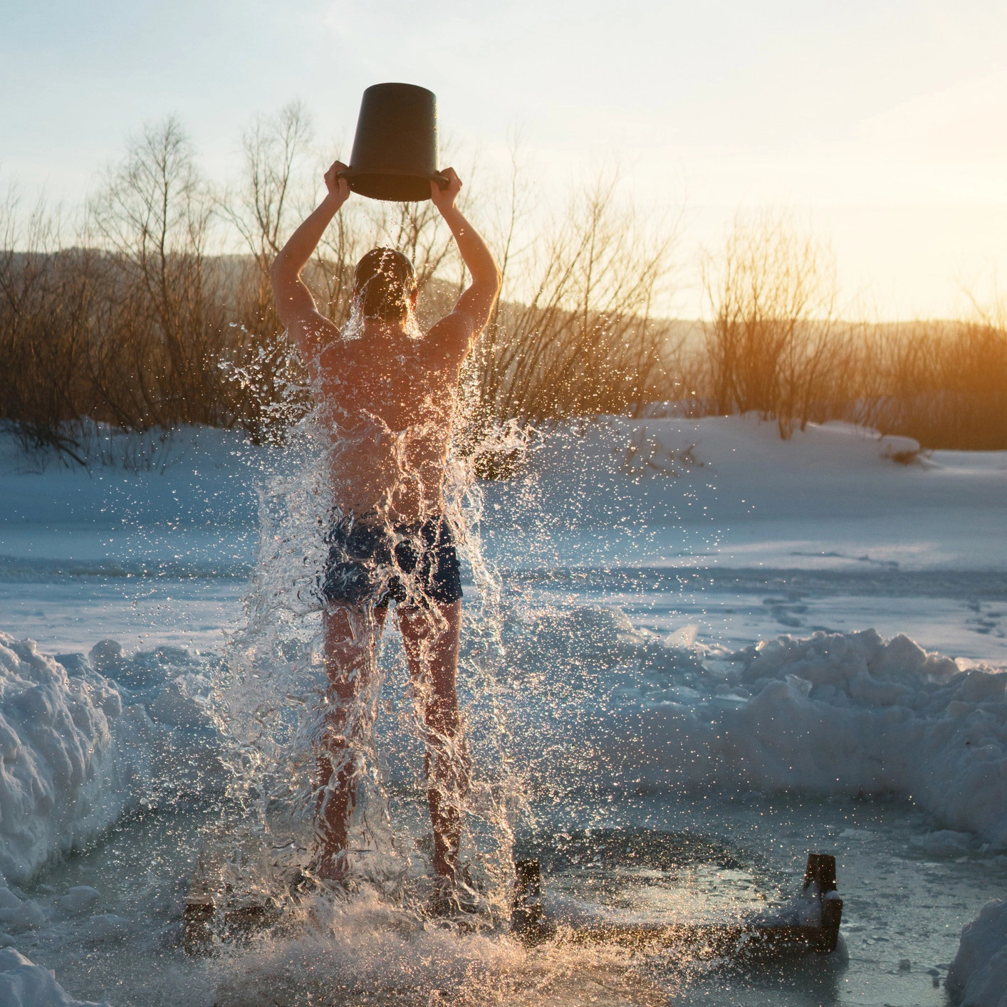 Ein Mann steht draußen im Winter und gießt sich kaltes Wasser aus einem Eimer über den Körper – eine Mischung aus Mutprobe und Erfrischung.