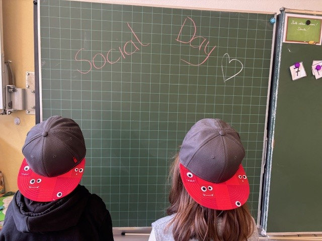 Foto zweier Kinder mit Kappen, die auf eine Tafel schauen wo "Social Day" steht