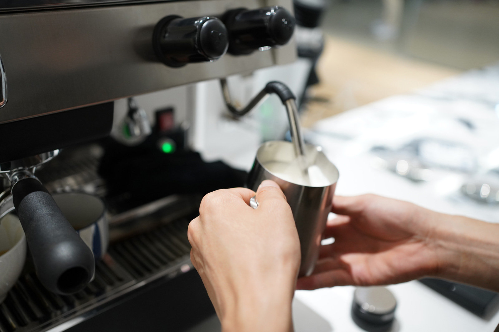 Hände sind zu sehen, die Milch aufschäumen an einer Kaffeemaschine
