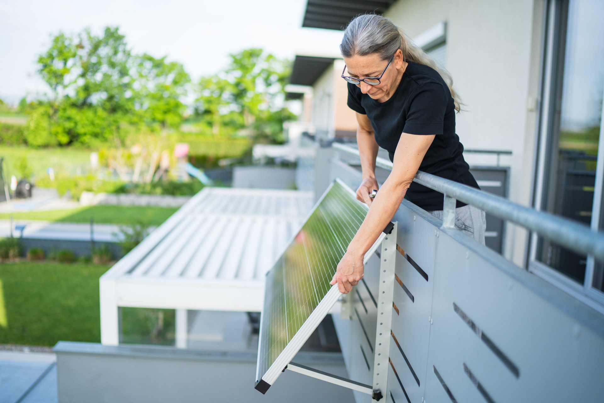Eine Frau richtet ein Solarpanel an ihrem Balkon aus. 