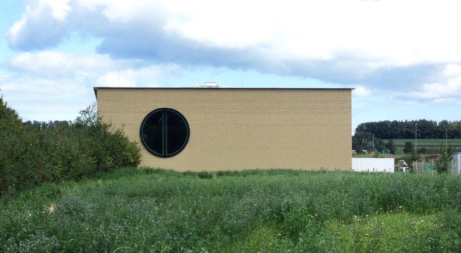 Kleines, niedriges Haus aus Stampflehm mit rundem Bullaugen-Fenster