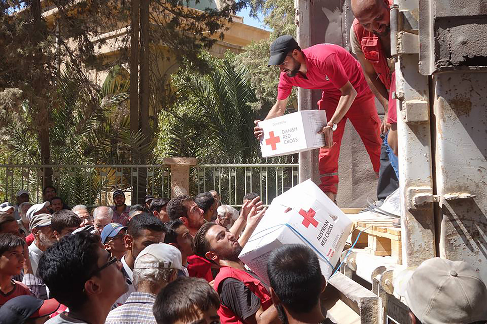 Syrien. Helfer des Syrisch Arabischen Roten Halbmondes verteilen Hilfspakete, die von anderen Rotkreuz-Gesellschaften zur  Verfügung gestellt werden. Paket mit Austrian Red Cross und Danish Red Cross. Abladen von einem LKW, Querformat