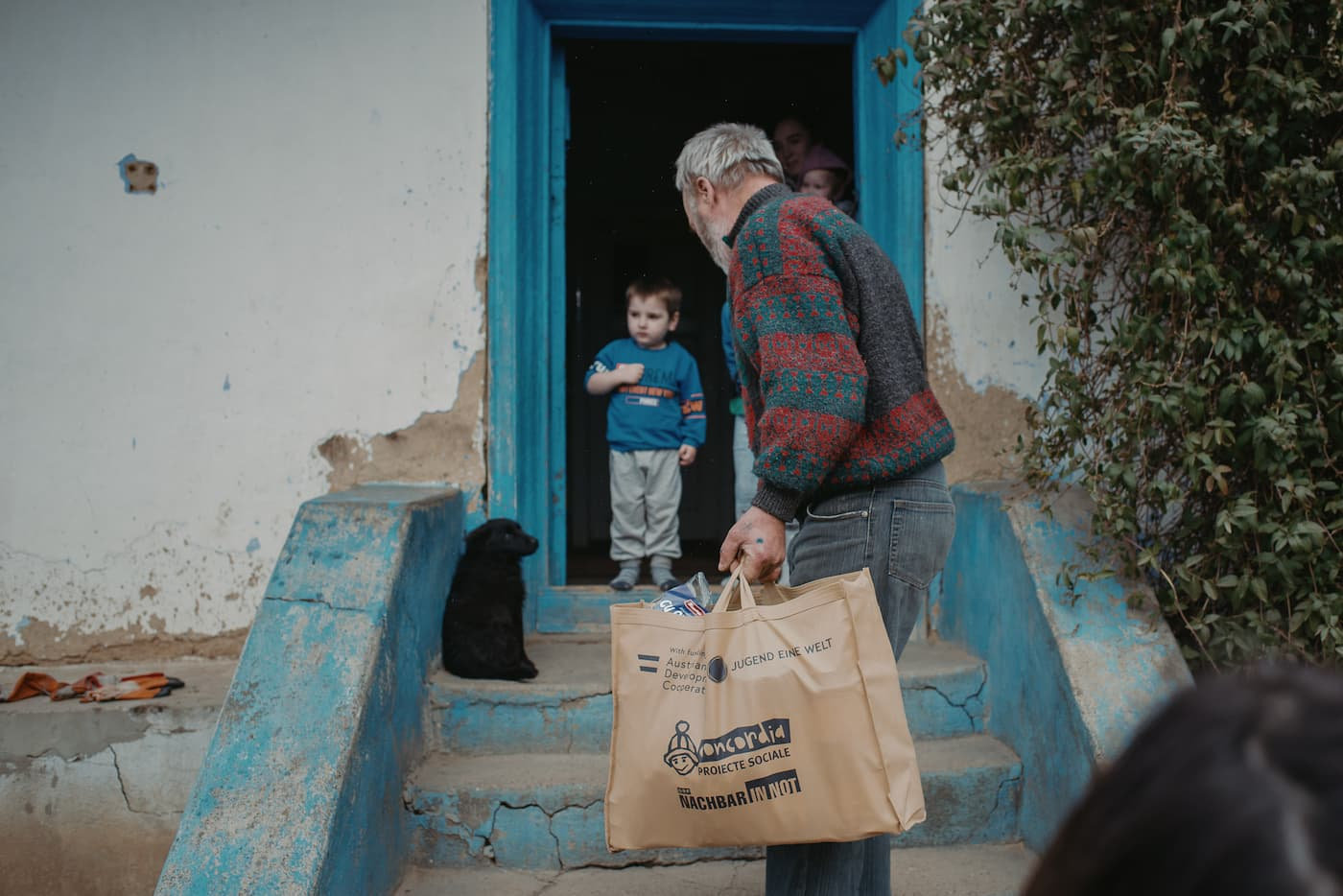 Ein alter Mann trägt gespendete Waren in ein ärmliches Haus.