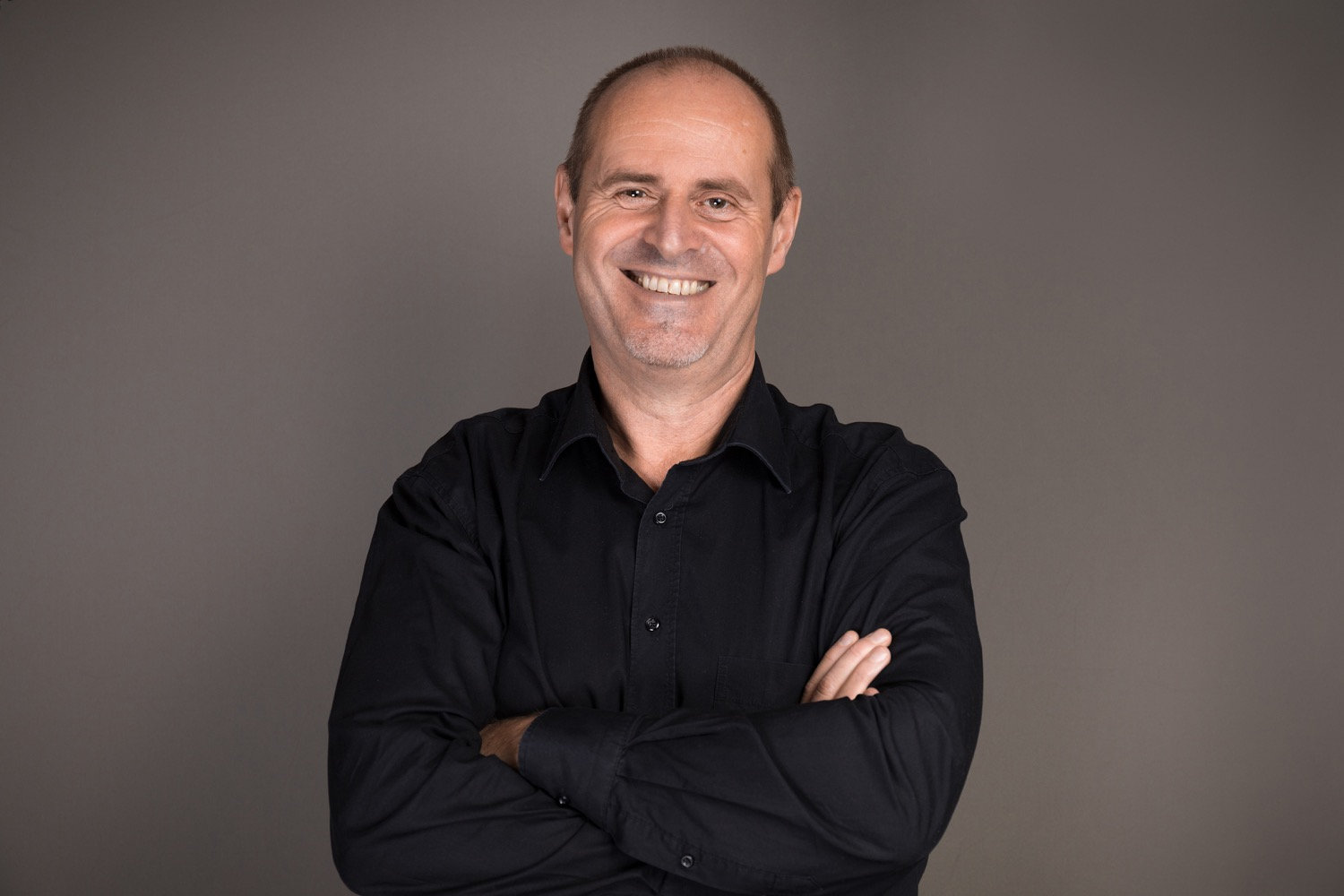 Lächelnder mittelalter Mann in schwarzem Hemd mit verschränkten Armen 