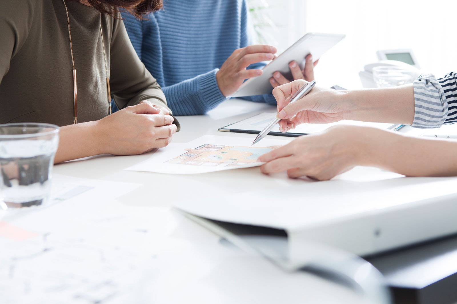 Drei Personen sitzen an einem Schreibtisch, um Verträge zu unterschreiben. 