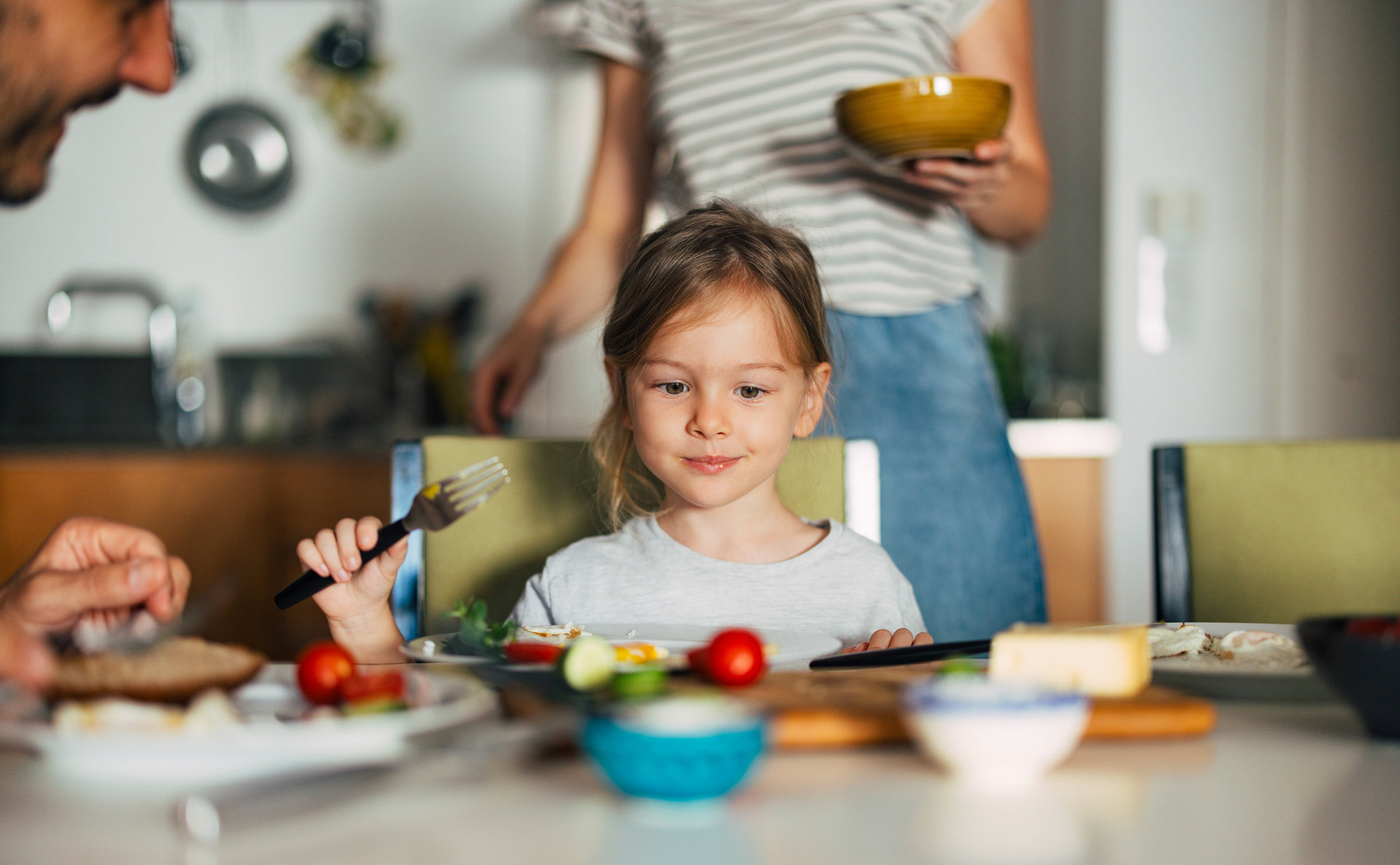 Ein Mädchen sitzt an einem Frühstückstisch und schaut sich die Lebensmittel an