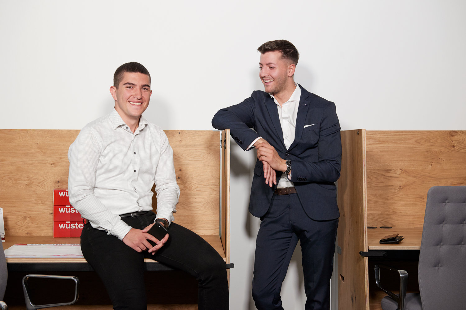 Zwei Männer in Anzügen an Schreibtische gelehnt