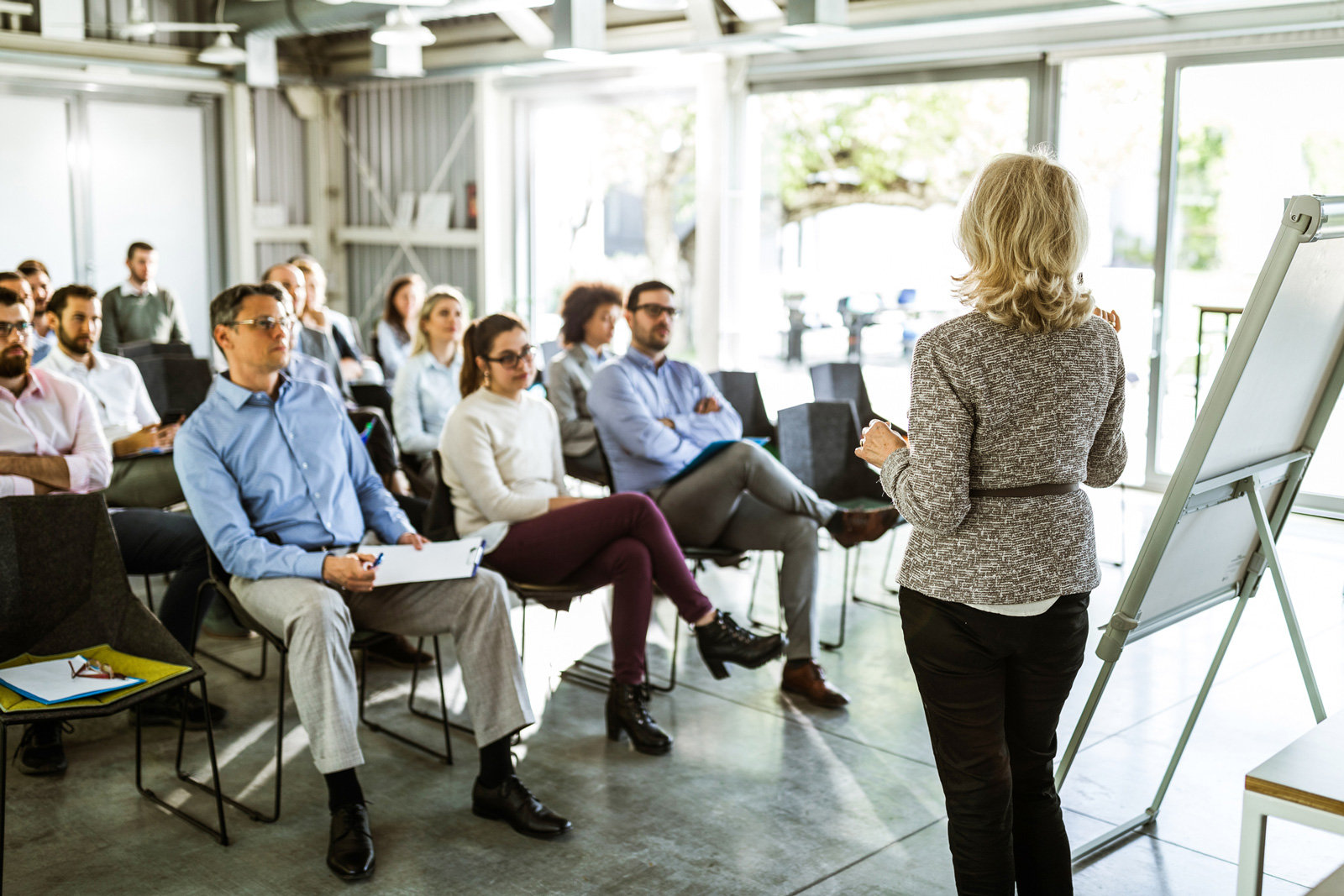 Das Bild zeigt eine Frau, die in einem Vortragssaal steht und gerade zum Publikum spricht