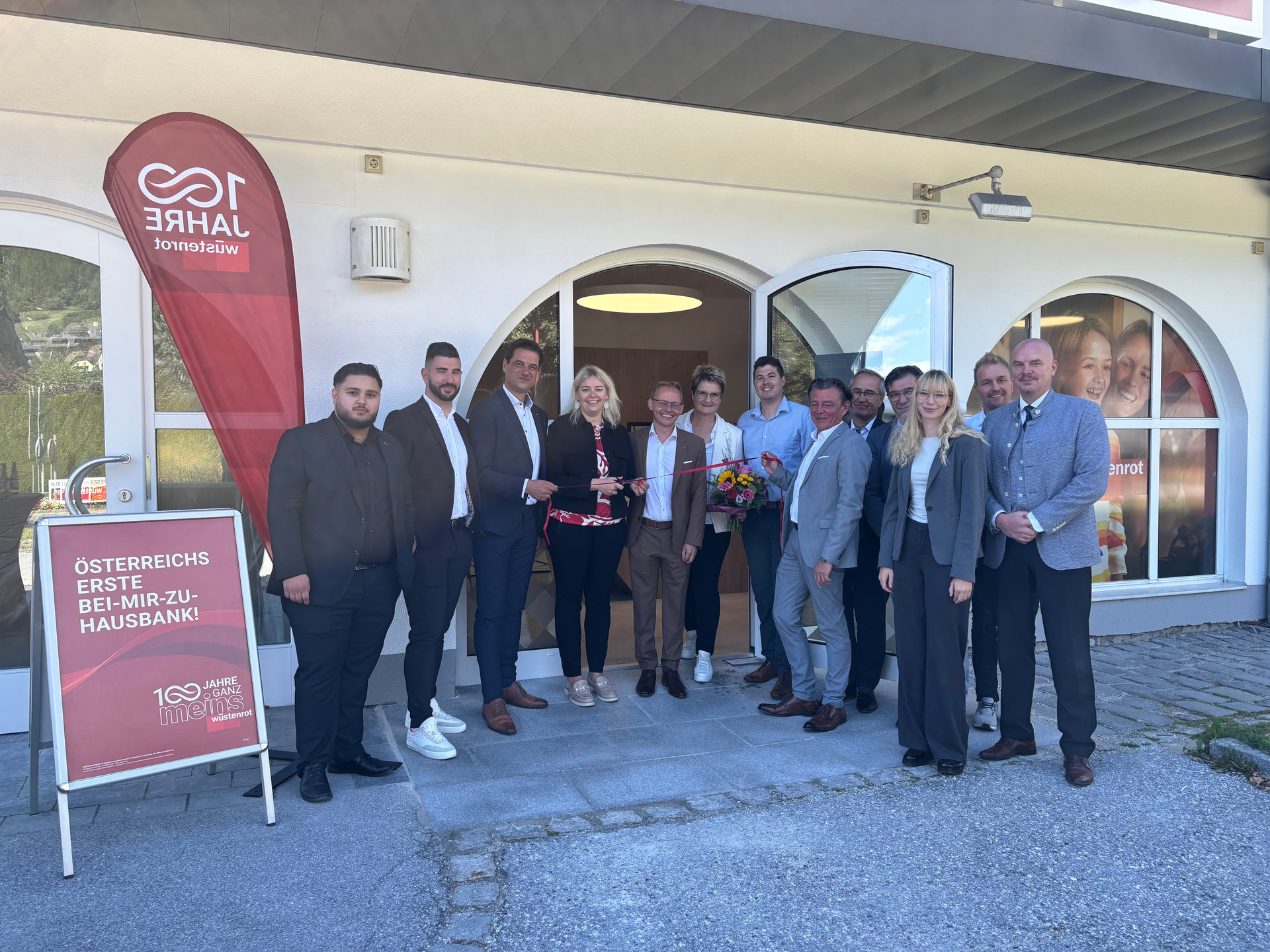 Gruppe von Menschen stehen vor einer neu eröffneten Wüstenrot Filiale. 