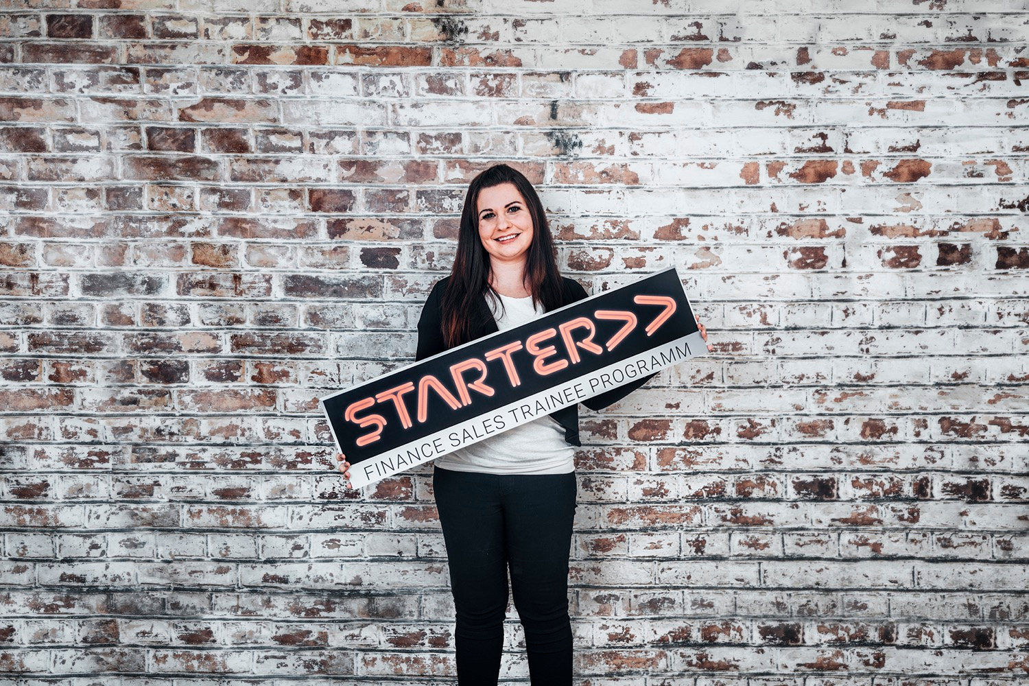 Frau mit einem Schild in der Hand, auf dem steht: "Starter >> Finance Sales Trainee Programm"