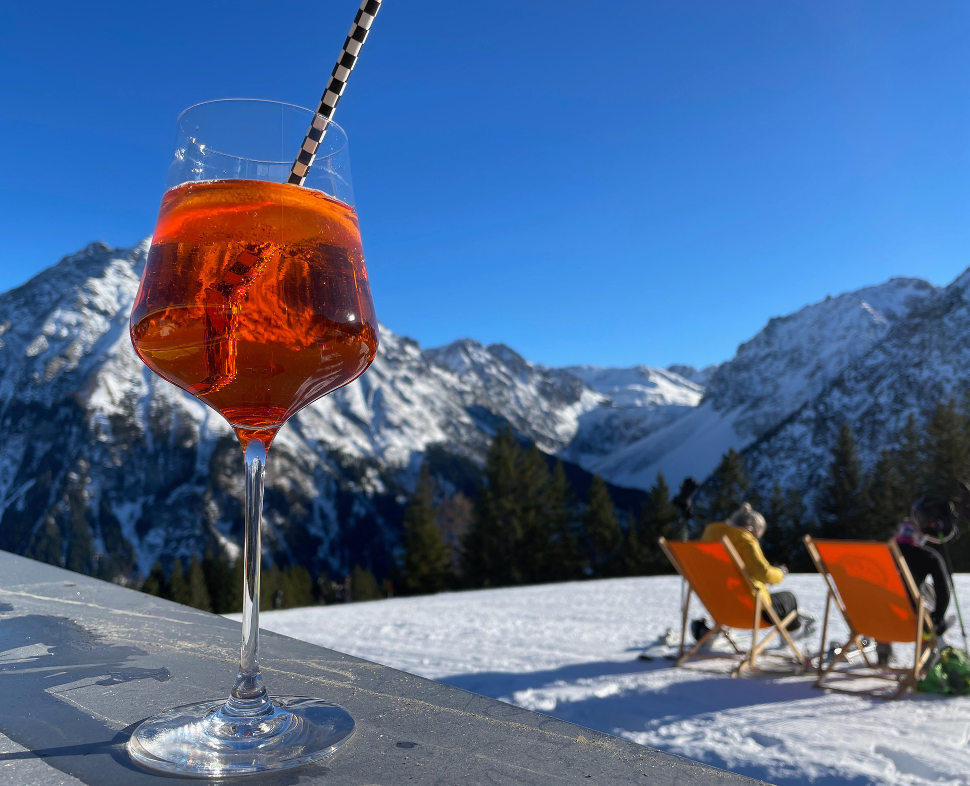 Glas mit rotem Getränk auf einem Tisch vor verschneiter Berglandschaft