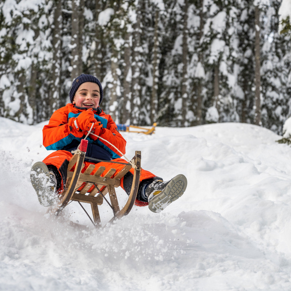 lachender Junge fährt auf einem Schlitten einen Abhang hinunter