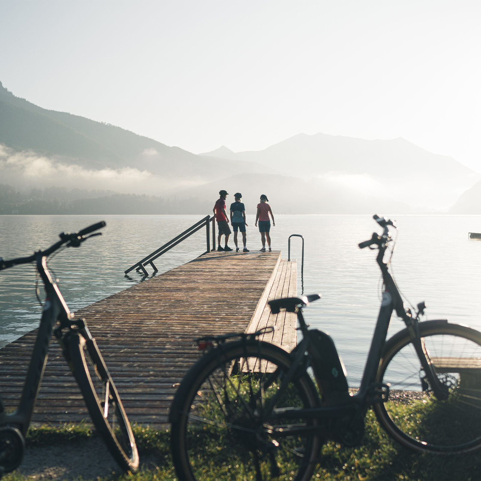 drei Menschen auf einem Steg in einem See im Gebirge