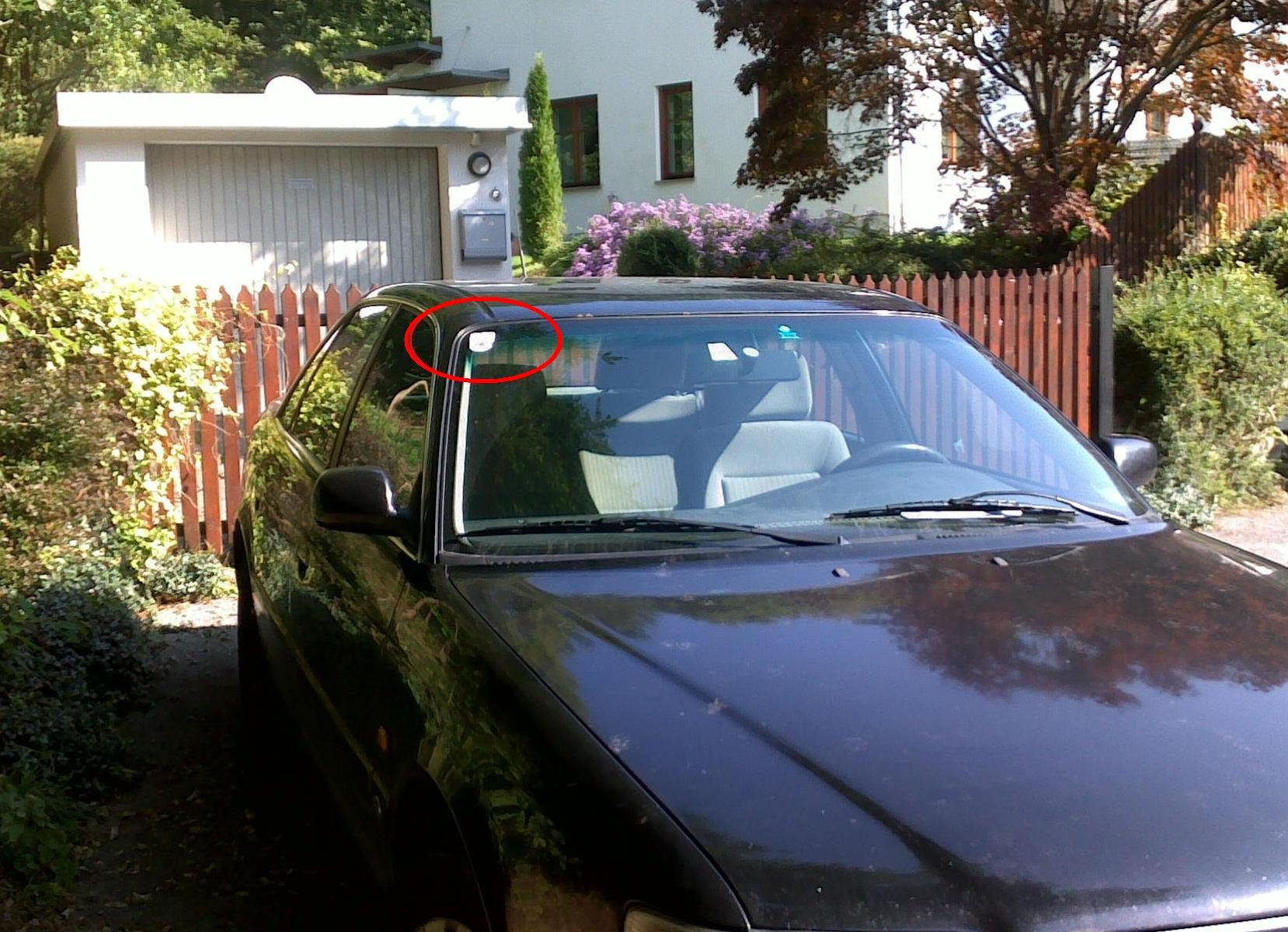 Schwarzes Auto geparkt in einer Einfahrt, ein roter Kreis umrundet einen Aufkleber.