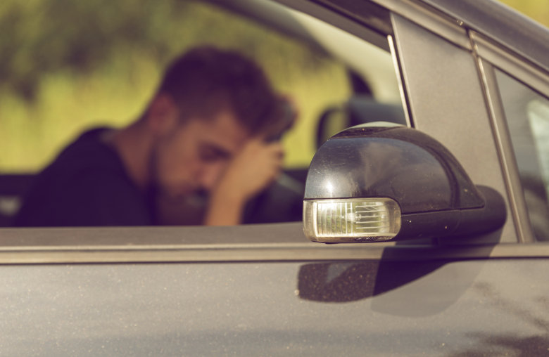 Ein Mann sitzt in seinem Auto und schläft auf dem Steuer.