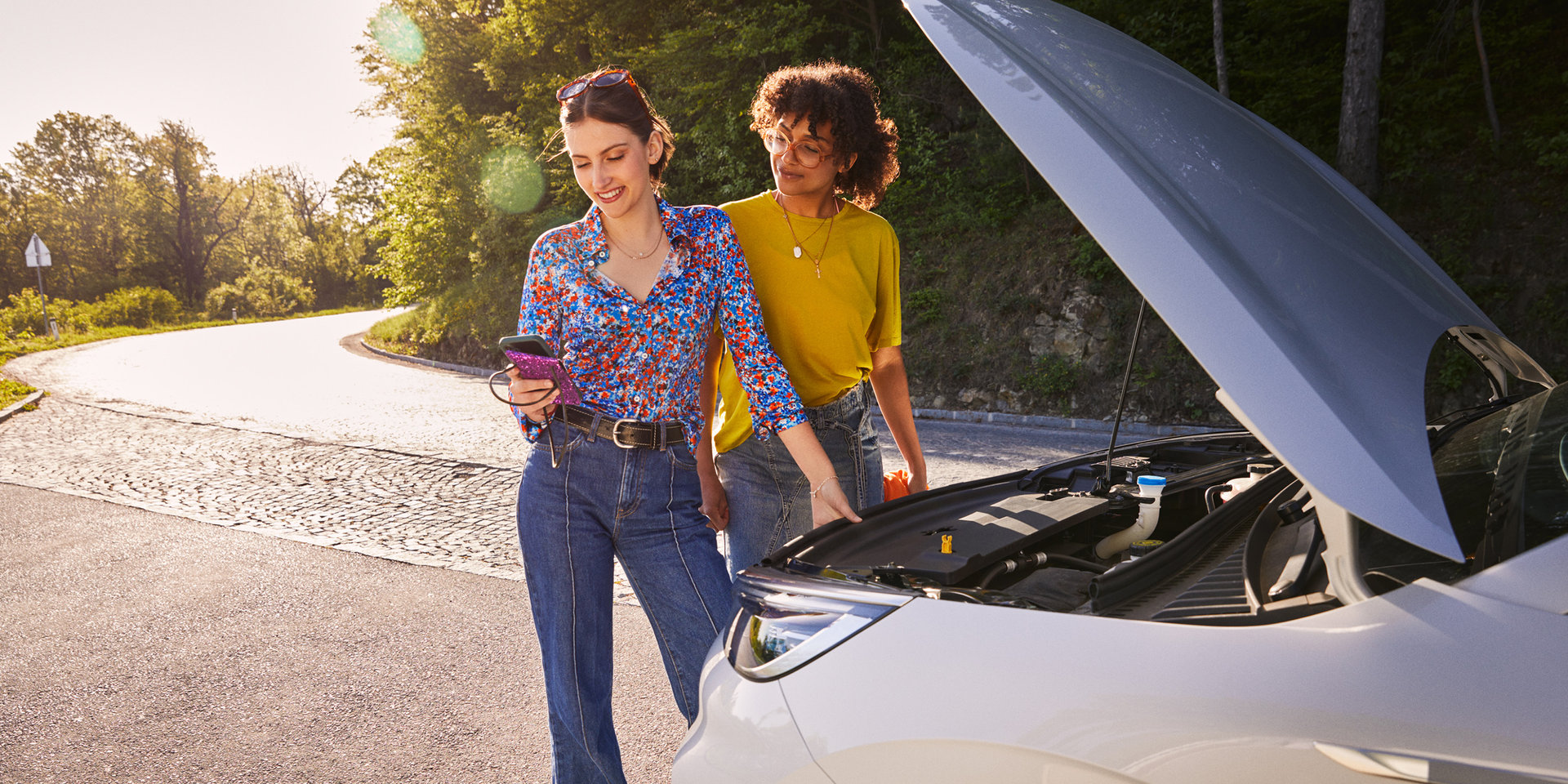 Zwei junge Frauen haben eine Autopanne und machen über ihr Smartphone eine Online-Schadensmeldung bei Wüstenrot. 