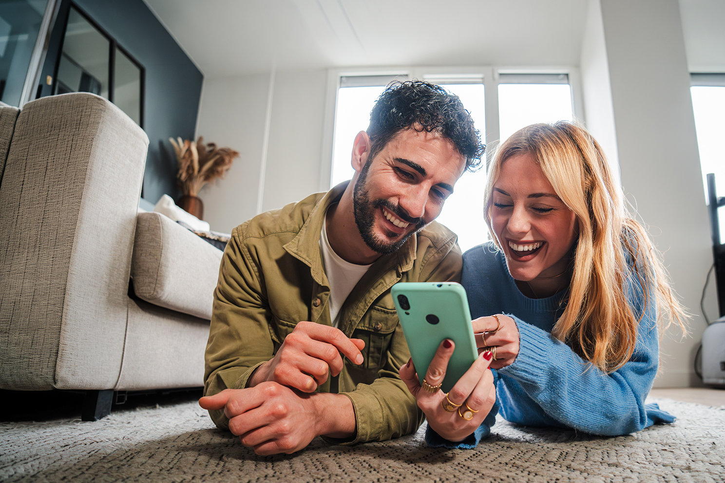 Zwei Personen liegen auf dem Boden und betrachten lächelnd gemeinsam ein Smartphone.