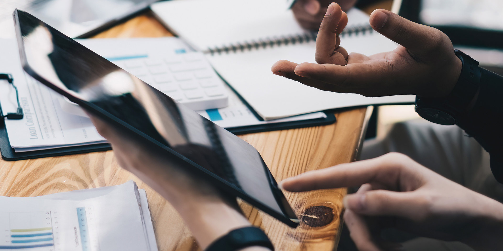 Auf einem Arbeitsschreibtisch sind viele Unterlagen und ein Tablet zu sehen.